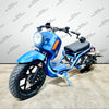 A blue gas ruckus style motorcycle with black wheels, a black seat, and orange signal lights, photographed indoors against a light gray wall with repeated watermark text.